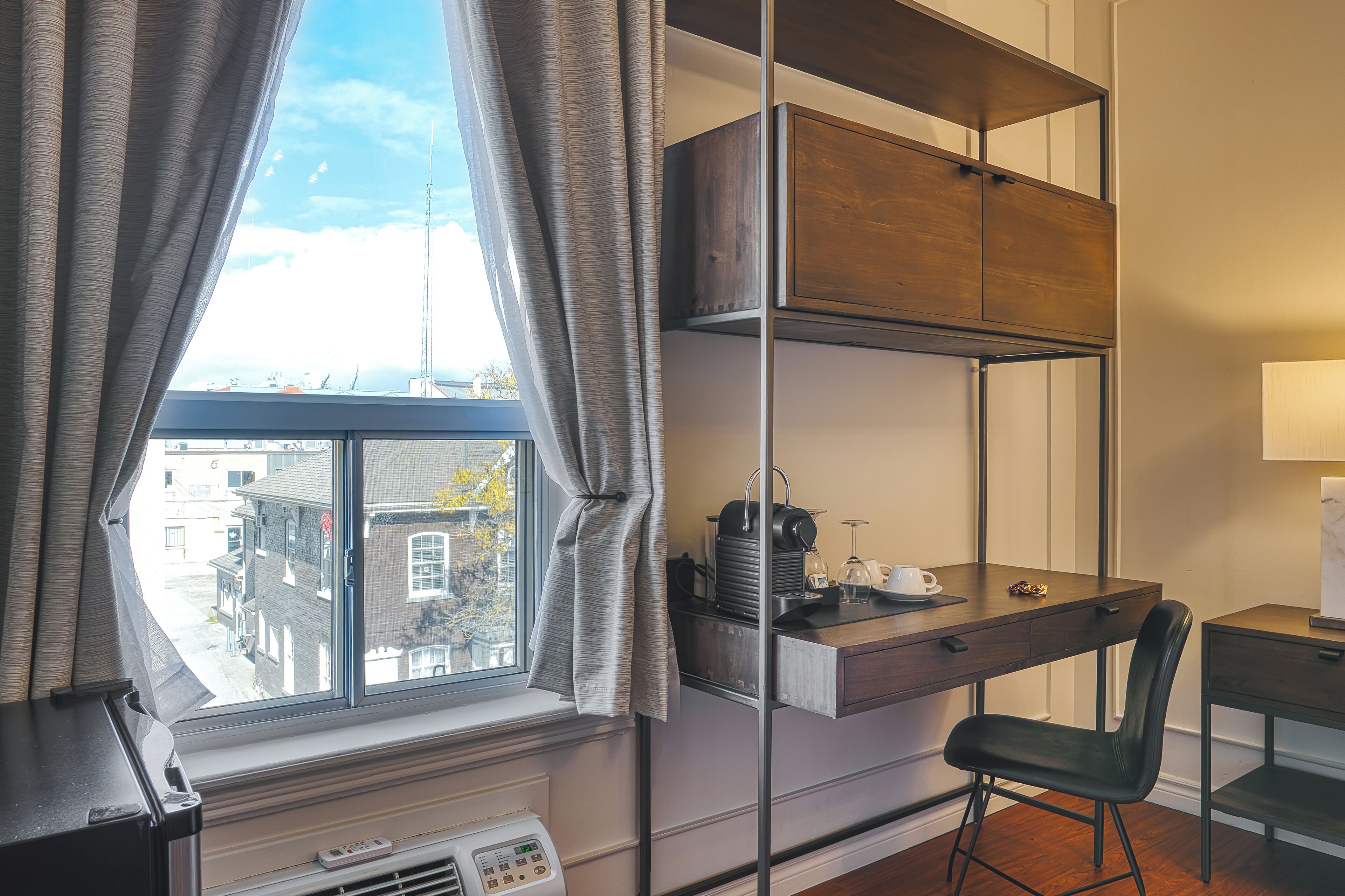 A modern room with a large window, a desk with a chair, a built-in shelf, and a radiator.