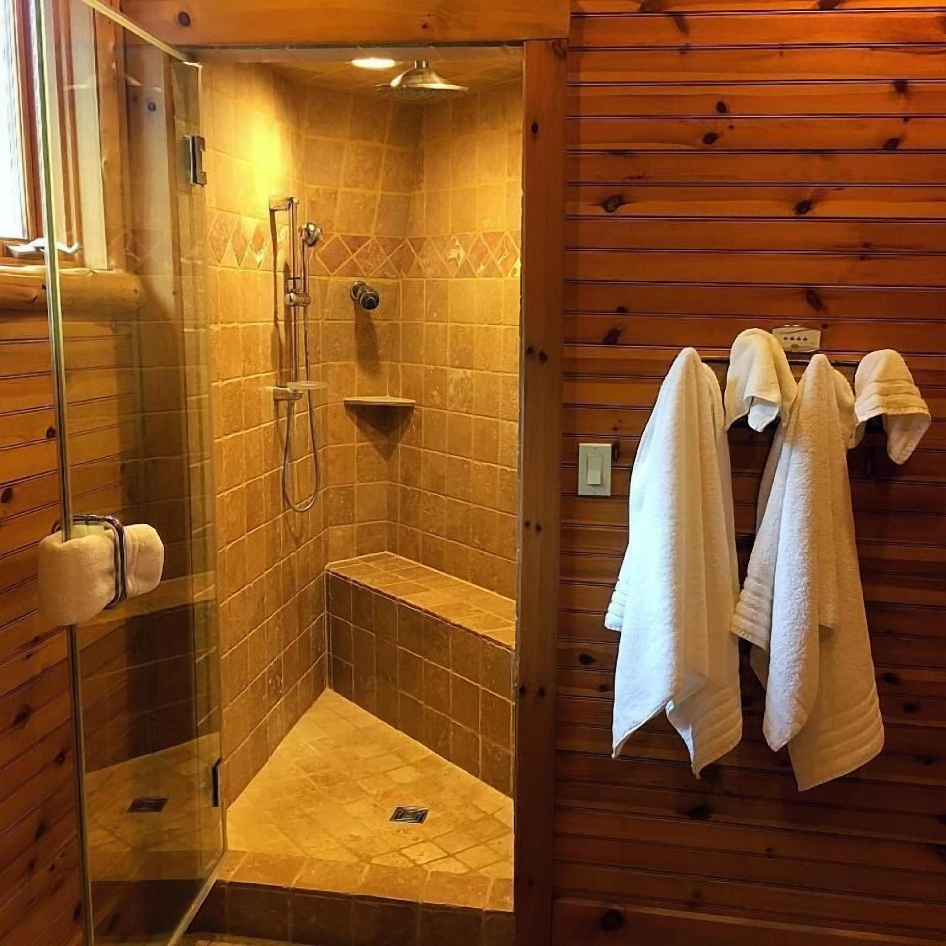 A shower area with a glass door, a bench, and towels hanging on the wall.