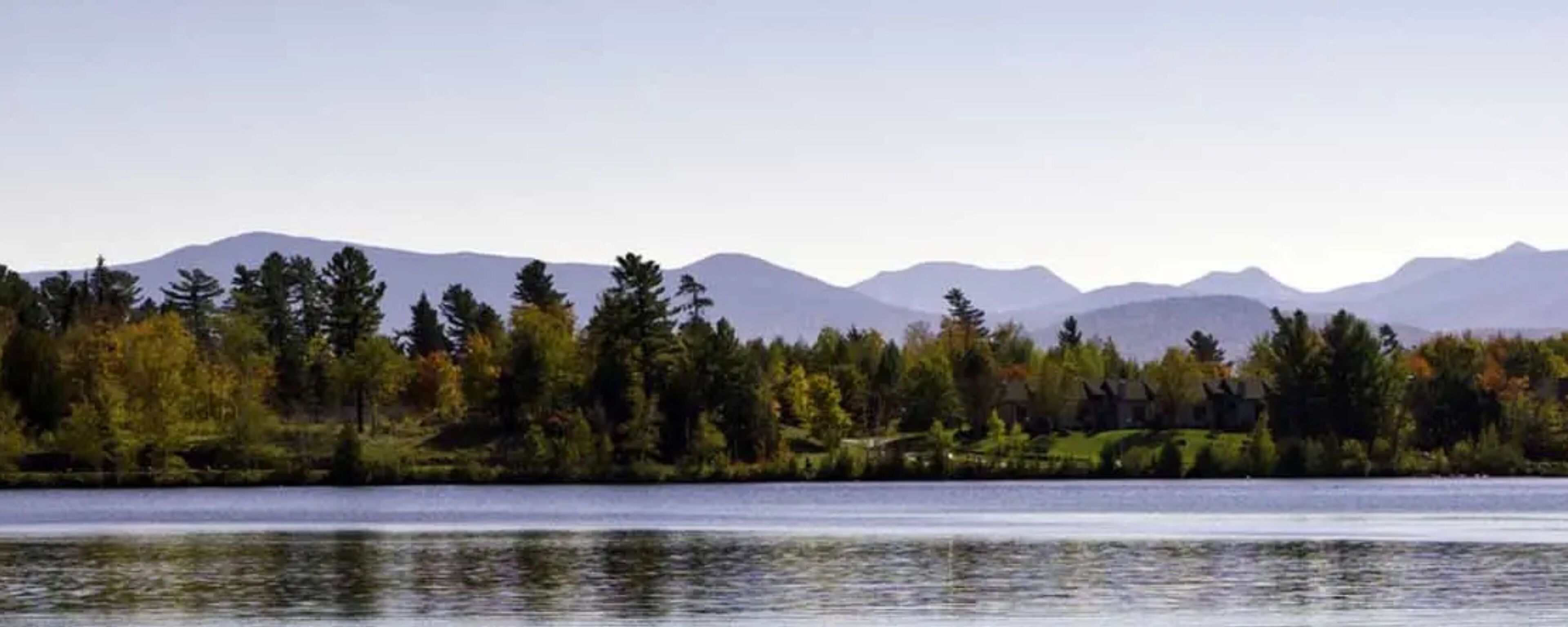 Une vue sur le lac, avec des montagnes en arrière-plan et une zone boisée parsemée de maisons.