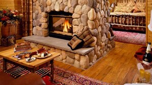 Ein gemütliches Zimmer mit Kamin aus Stein, einer bequemen Couch und einem Tisch mit Büchern und Snacks.