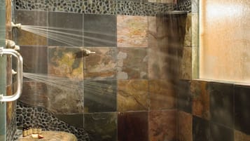 A stone-walled shower with a rain showerhead, a towel rack, and a small rock on the floor.