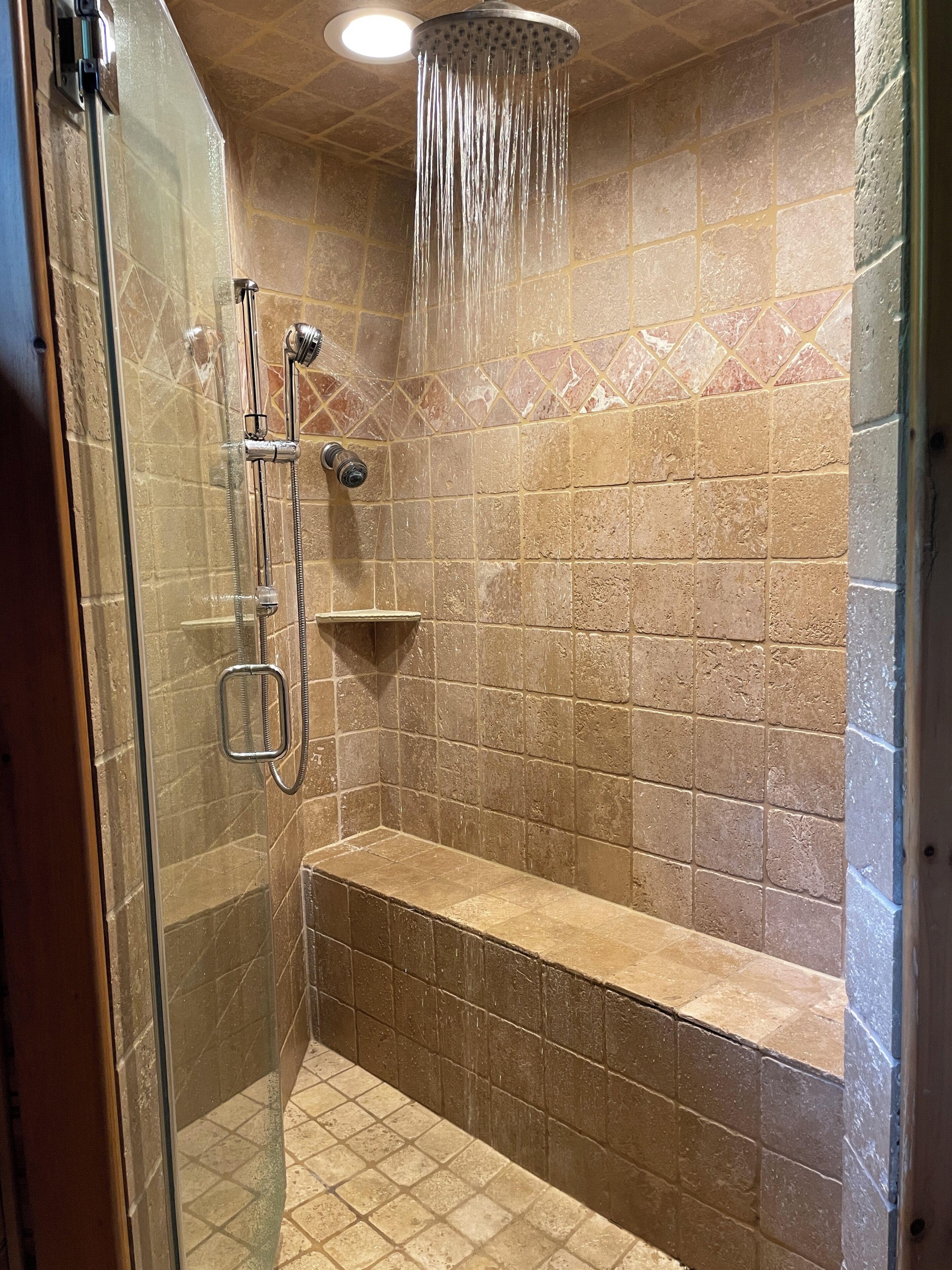 A shower with a handheld showerhead, a wall-mounted faucet, and a bench.