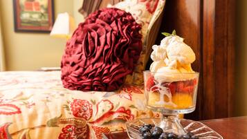 A dessert in a glass bowl on a table, with a bed and a red pillow in the background.