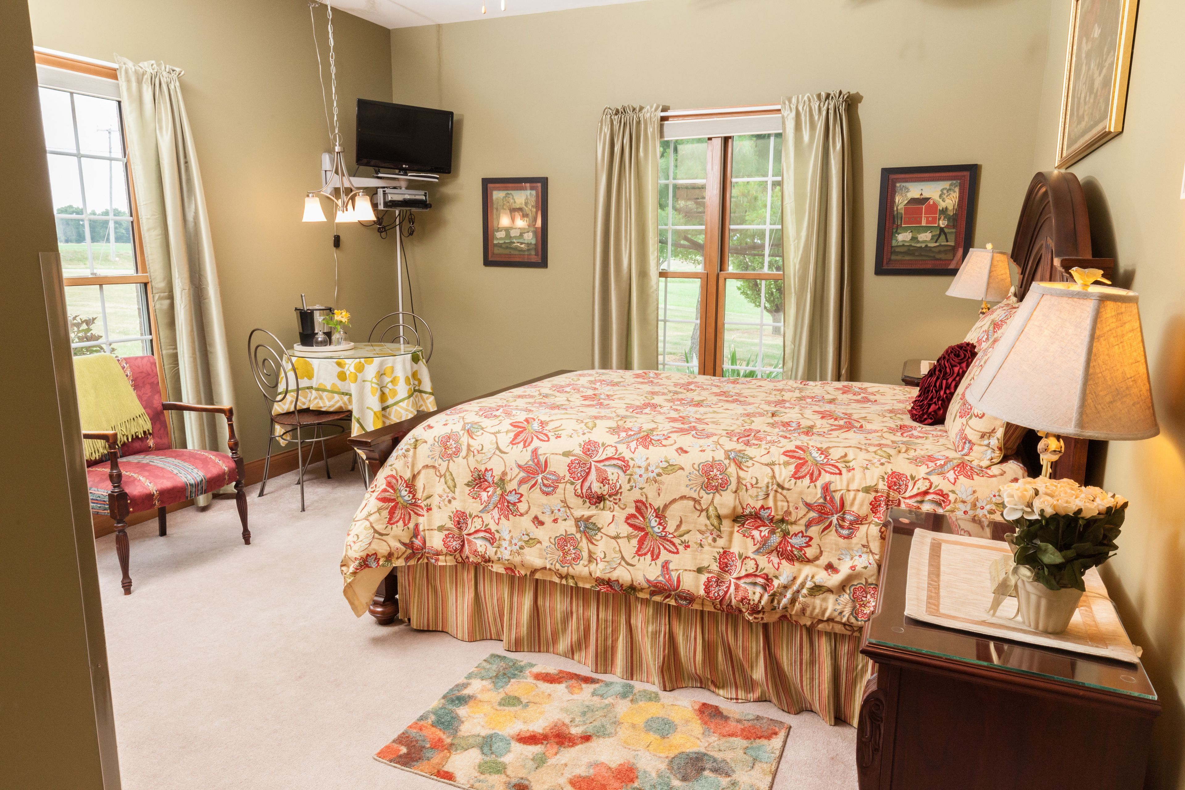 A bedroom with a large bed, a desk with a chair, a television, and a window with curtains.