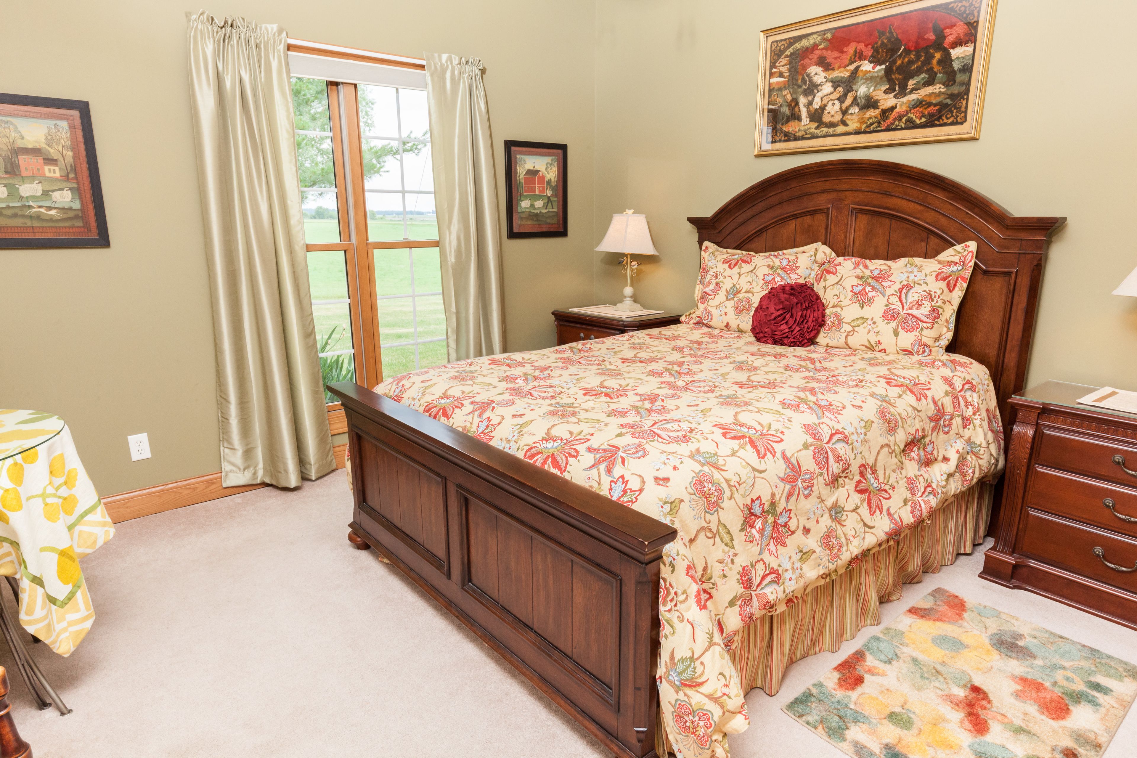 Een slaapkamer met een groot bed, een nachtkastje, een dressoir, een raam met gordijnen en een deur naar een balkon.