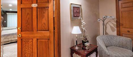 A room with a wooden door labeled "Loft," a small table with a lamp and a plant, a patterned armchair, and a framed picture on the wall.