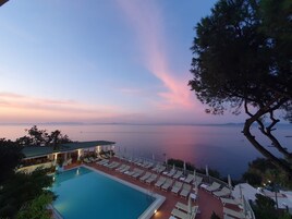 Zona de piscina con sillones reclinables y sombrillas, con vista a una masa de agua al atardecer.