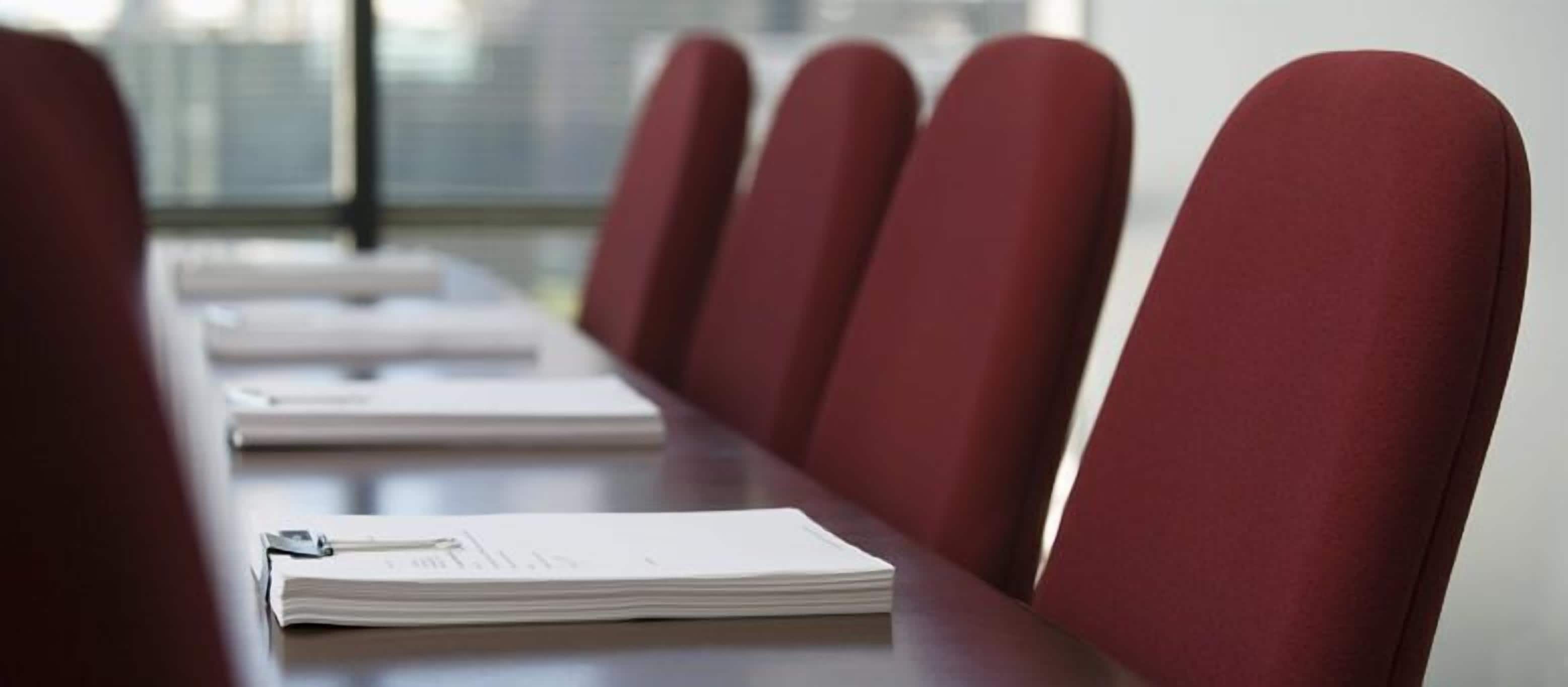 A conference room with a long table and red chairs.