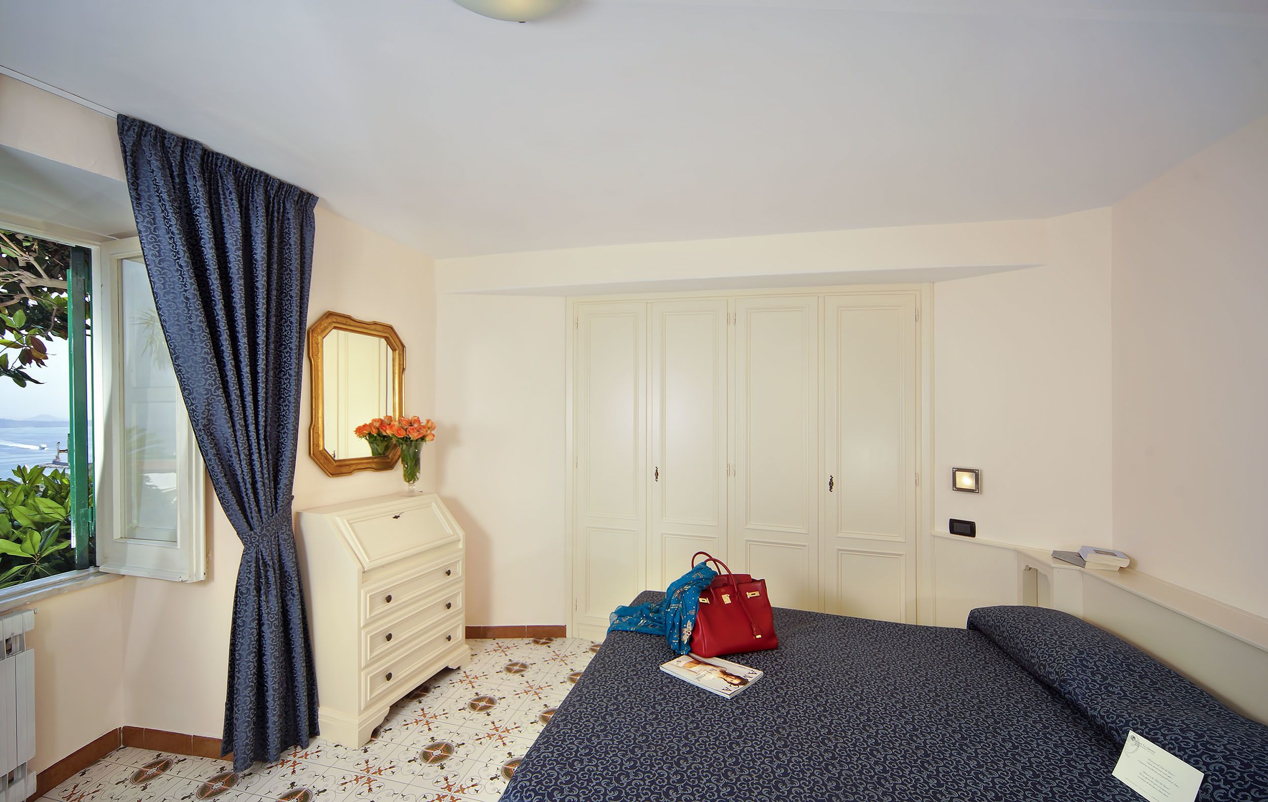 A bedroom with a bed, a dresser, a mirror, a window with curtains, and a view of the outdoors.