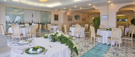 A banquet hall with round tables, white tablecloths, and floral centerpieces.