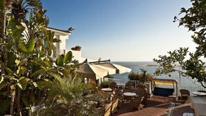 A terrace with outdoor seating, a view of the sea, and lush tropical plants. - Le Querce Resort Sea Thermae & SPA (Ischia)