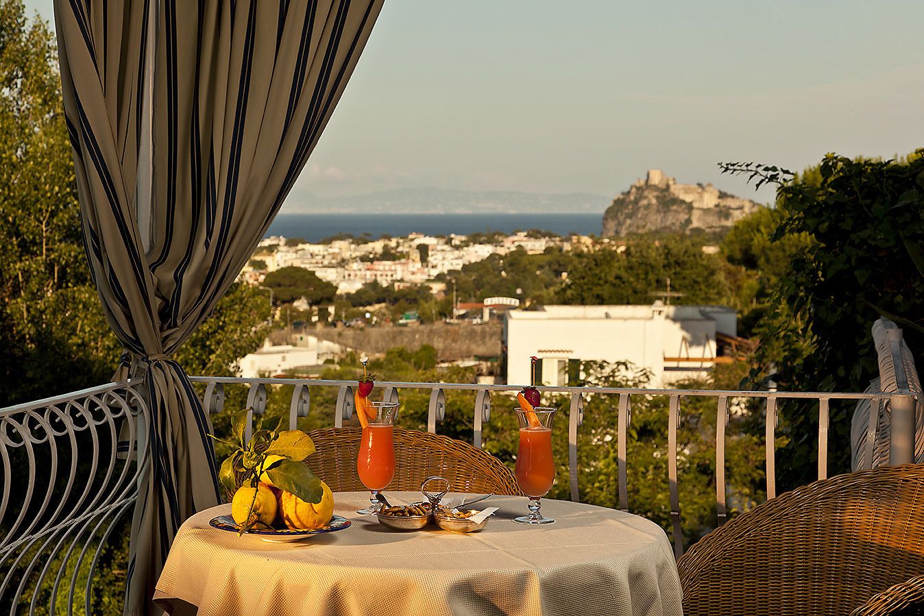Un balcon avec une table dressée pour deux personnes, offrant une vue sur une ville côtière et un château.