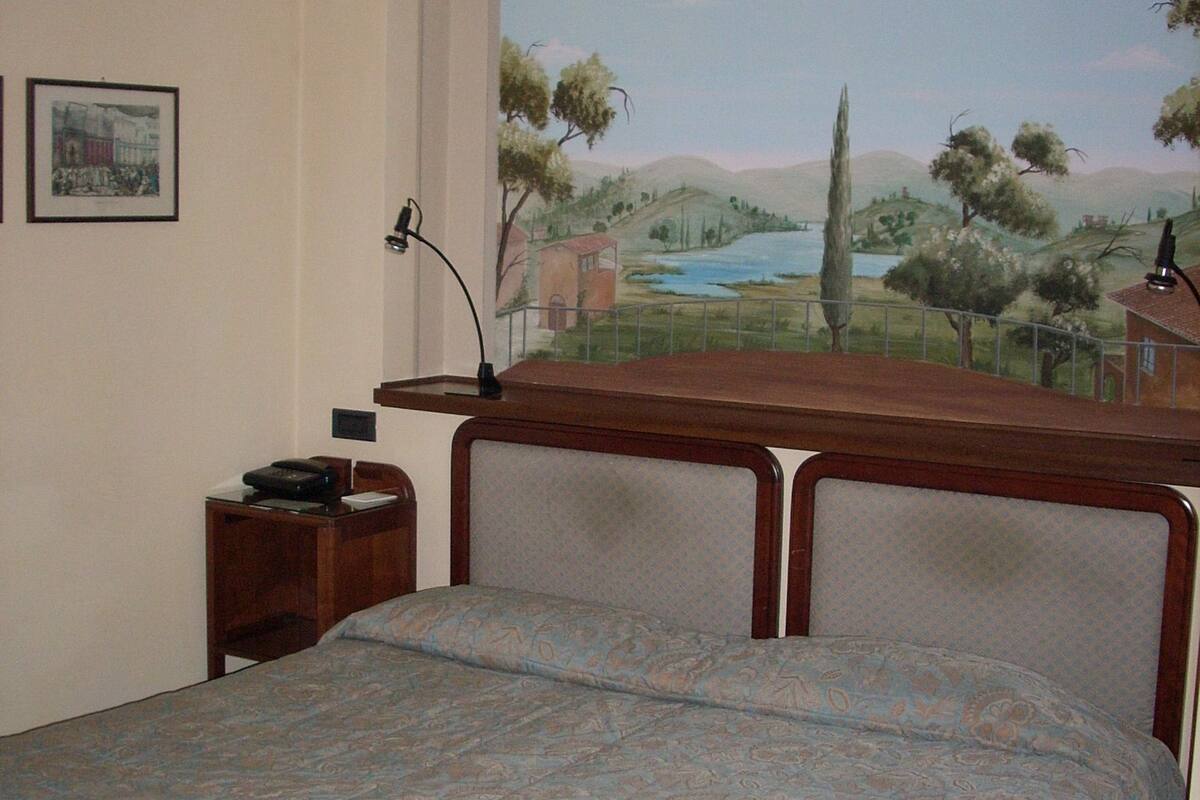 A bedroom with a bed, a nightstand, a lamp, and a mural of a landscape on the wall.