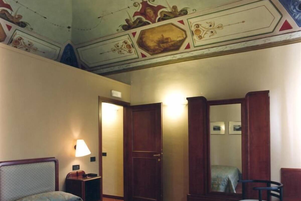 A hotel room with a bed, a chair, a desk, and a wardrobe.