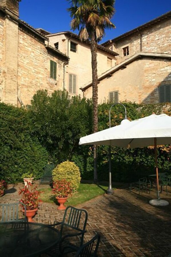 Un patio con edificios de piedra, una palmera y mobiliario exterior con una sombrilla blanca.