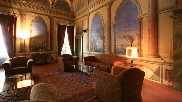 Una habitación lujosa con un amplio ventanal de arco, un techo ricamente decorado y una chimenea clásica.