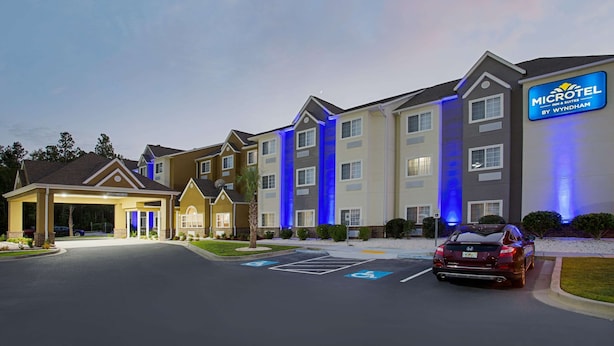 A Microtel Inn Suites by Wyndham with a parking lot and a red car parked in front. - Microtel Inn & Suites by Wyndham Walterboro (Walterboro)