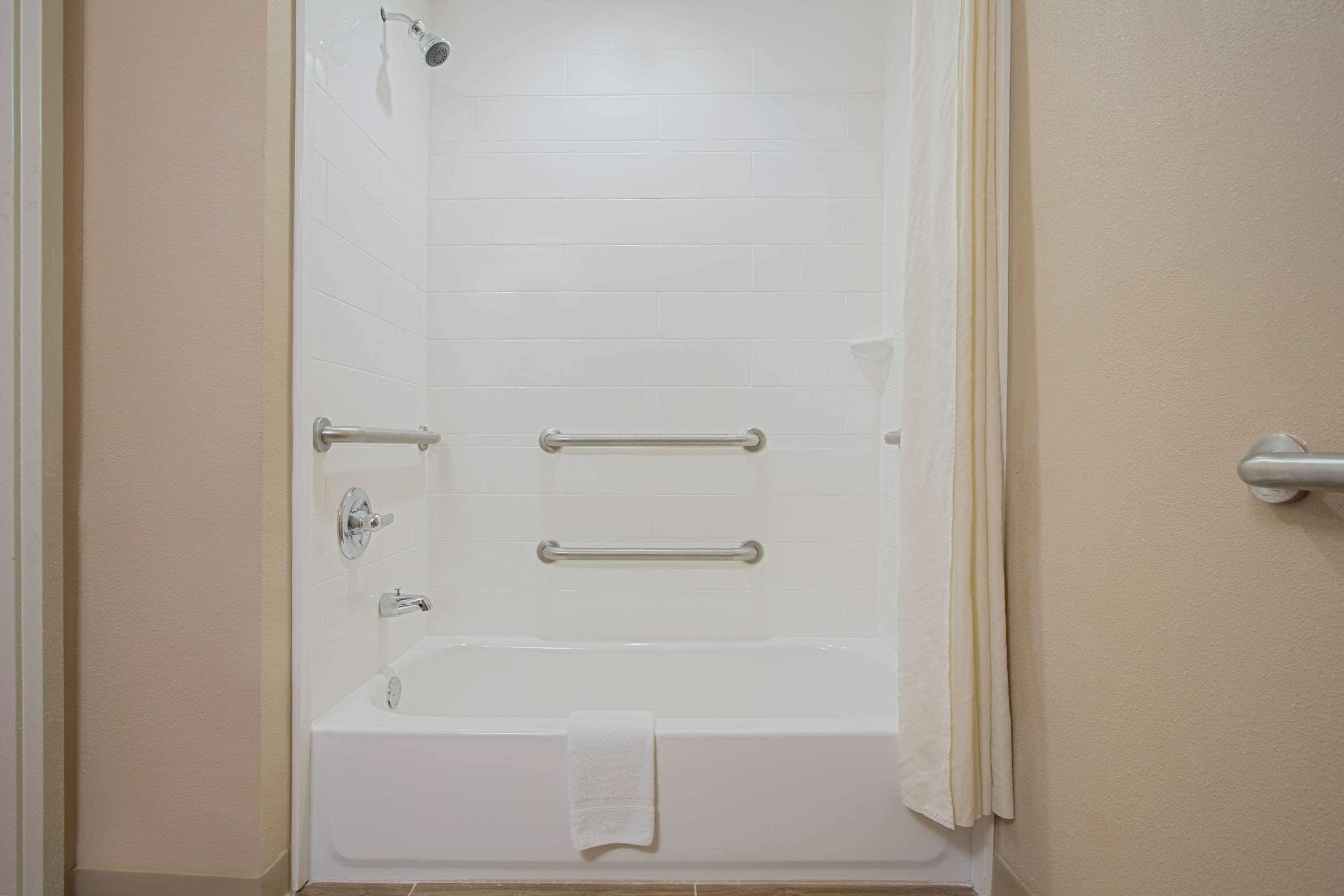 A bathroom with a bathtub, grab bars, and a showerhead.