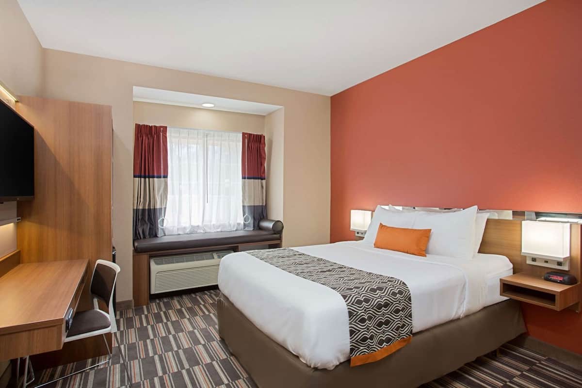 A hotel room with a bed, desk, chair, window with curtains, and a TV.