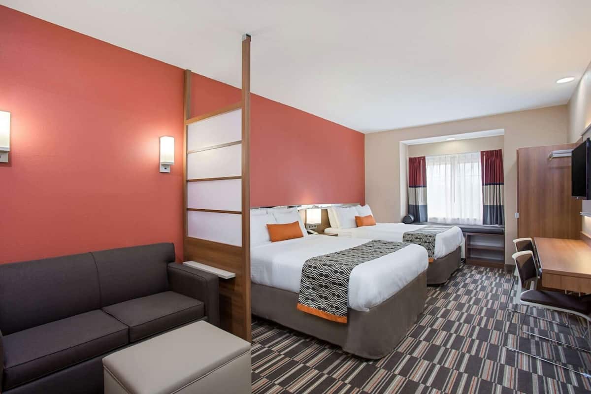 A hotel room with a sofa, two beds, a desk, and a TV.