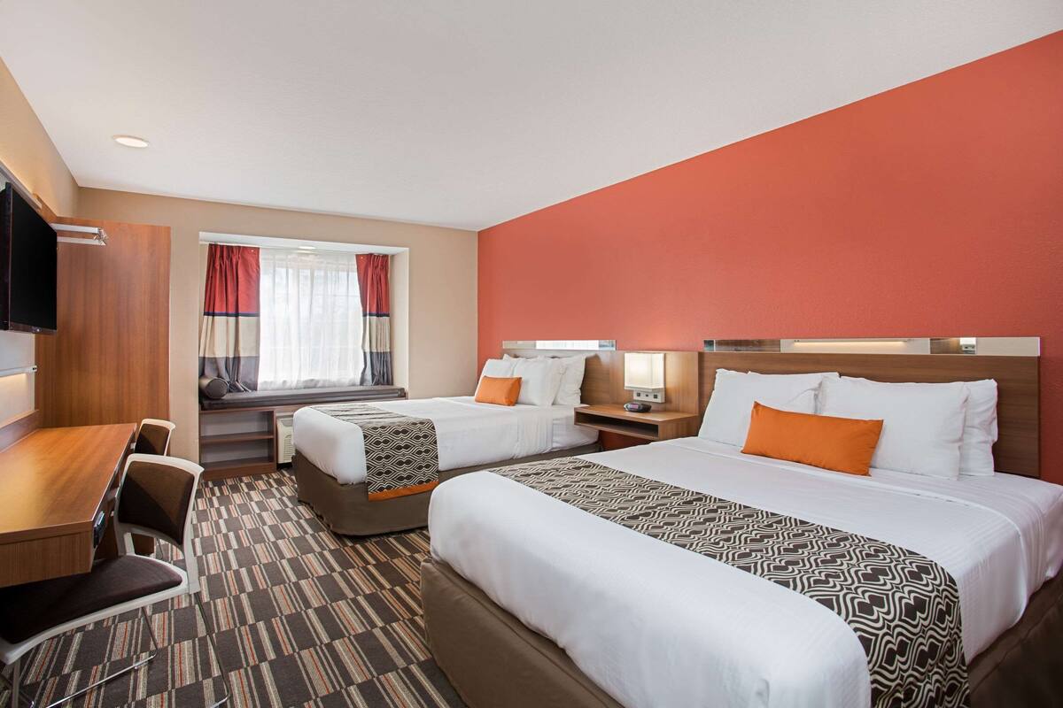 A hotel room with two beds, a desk, and a TV.