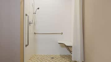 A shower with a white tiled wall, a grab bar, and a shower seat.