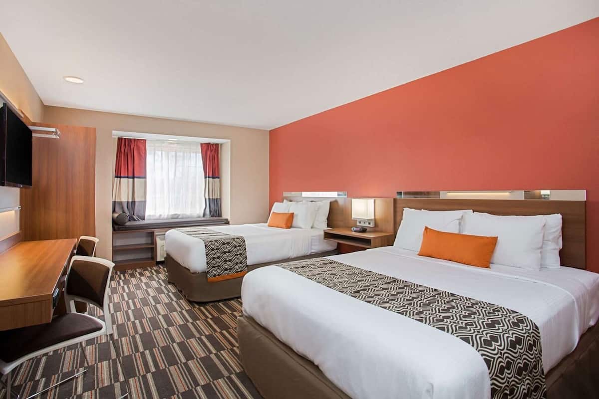 A hotel room with two beds, a desk, a chair, a TV, and a window with curtains.