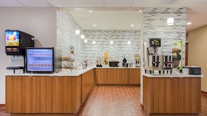 A modern hotel lobby with wooden counters, a digital screen, a coffee machine, and a tiled floor. - Microtel Inn & Suites by Wyndham Walterboro (Walterboro)