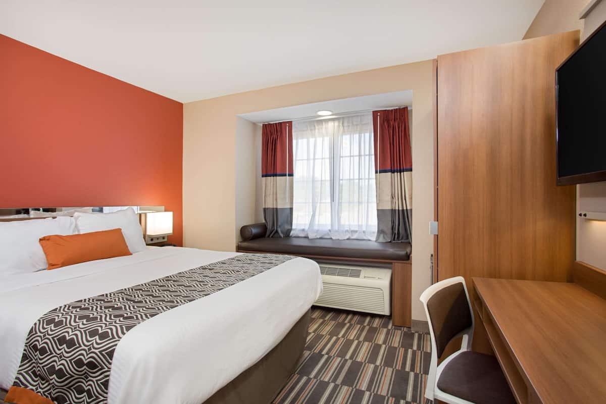 A hotel room with a large bed, a desk, a chair, a window with curtains, and a television.