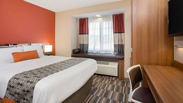 A hotel room with a large bed, a desk, a chair, a window with curtains, and a television.