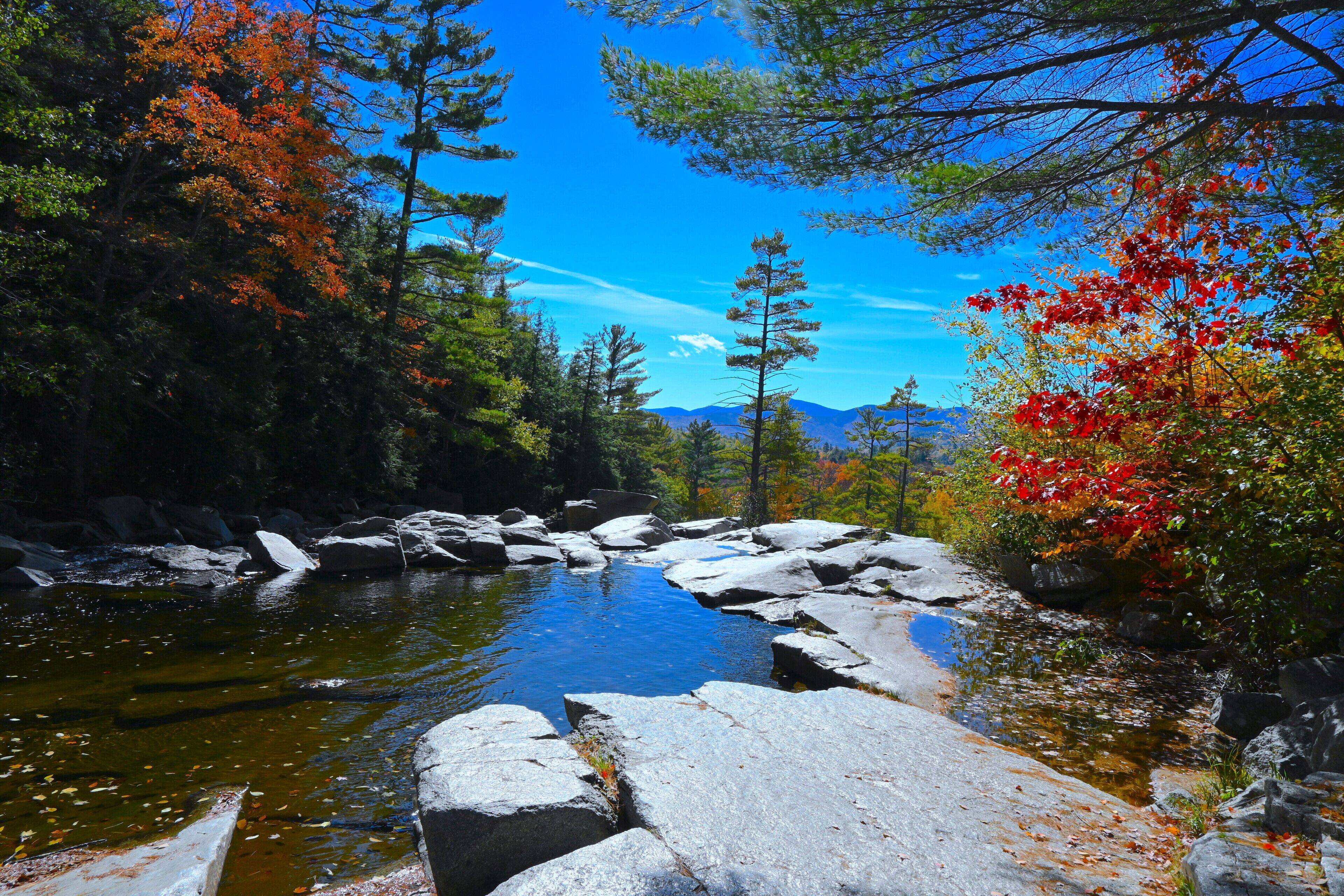 A natural landscape with a clear stream, rocky terrain, and autumn foliage.