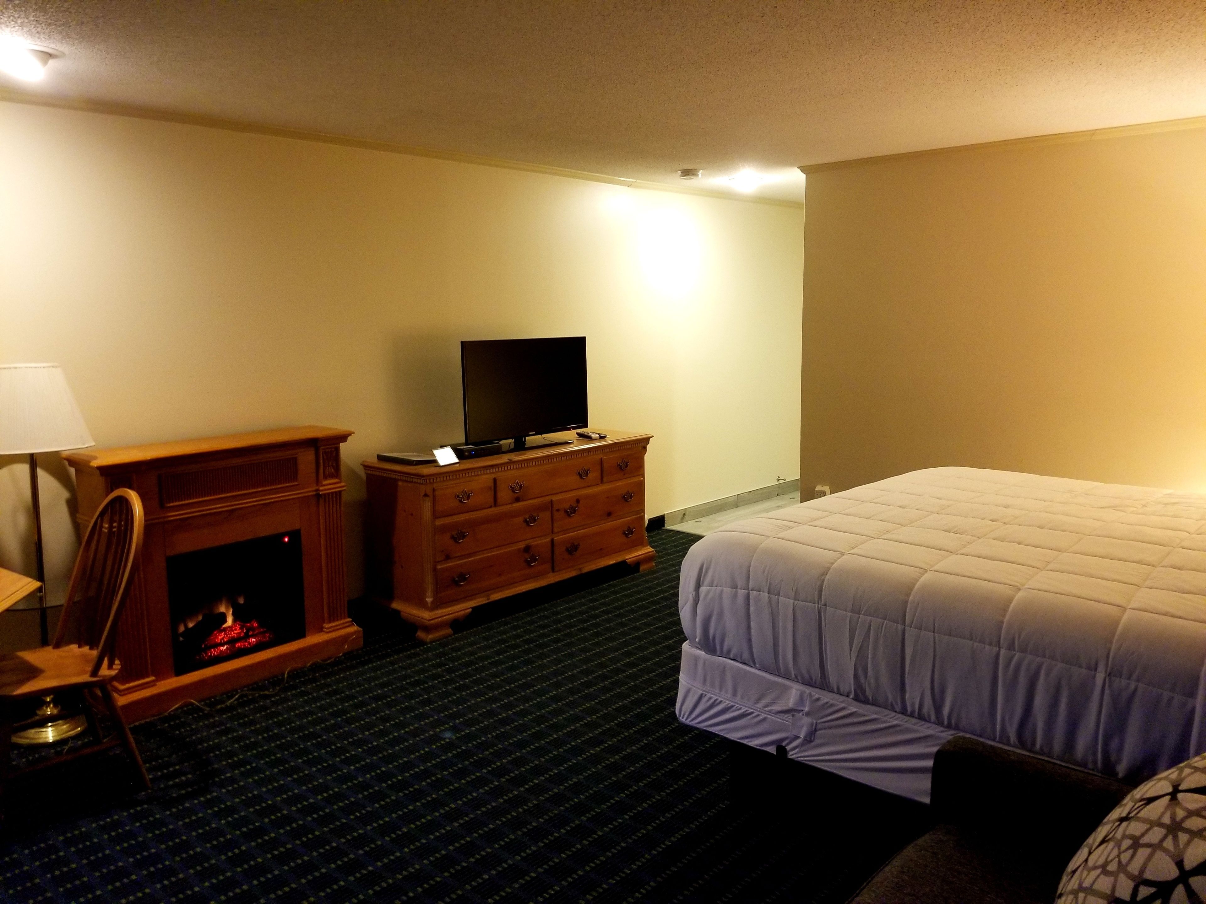 A hotel room with a bed, a dresser, a television, and a fireplace.