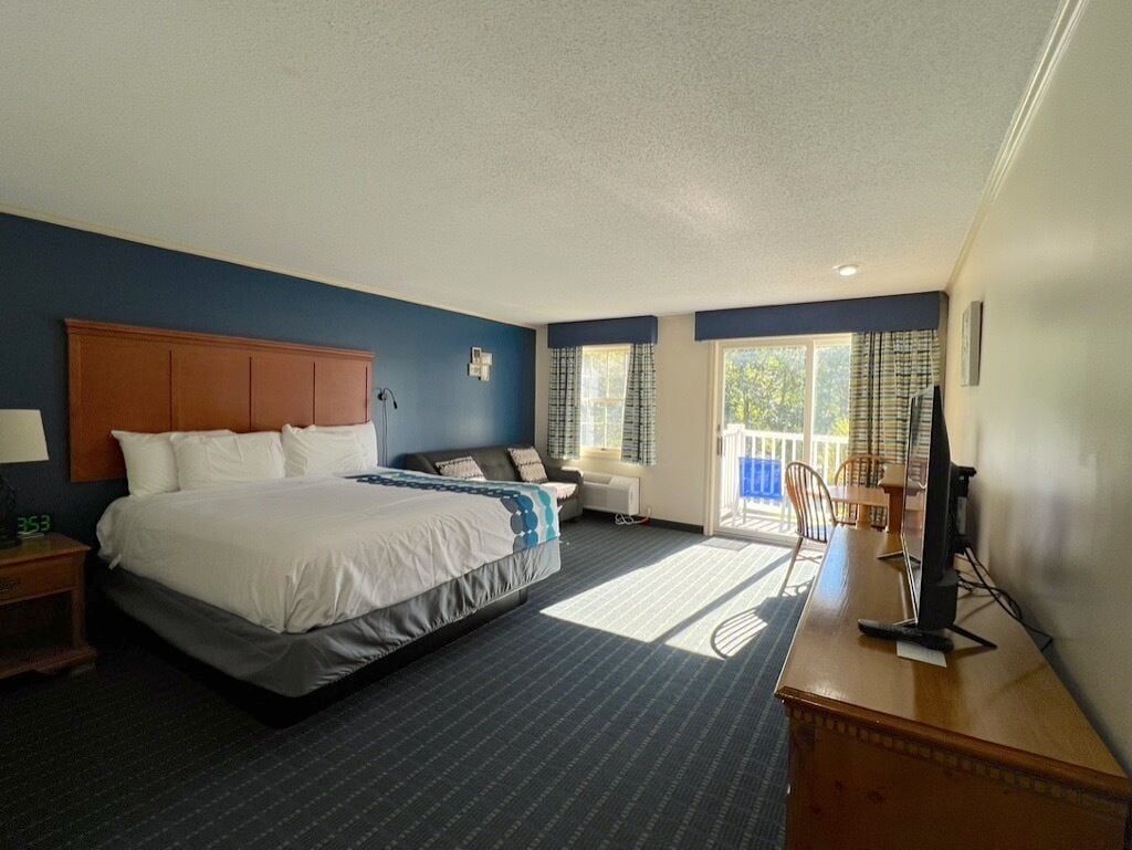 Una habitación de hotel con una cama grande, un escritorio con ordenador, una silla y una ventana con cortinas.