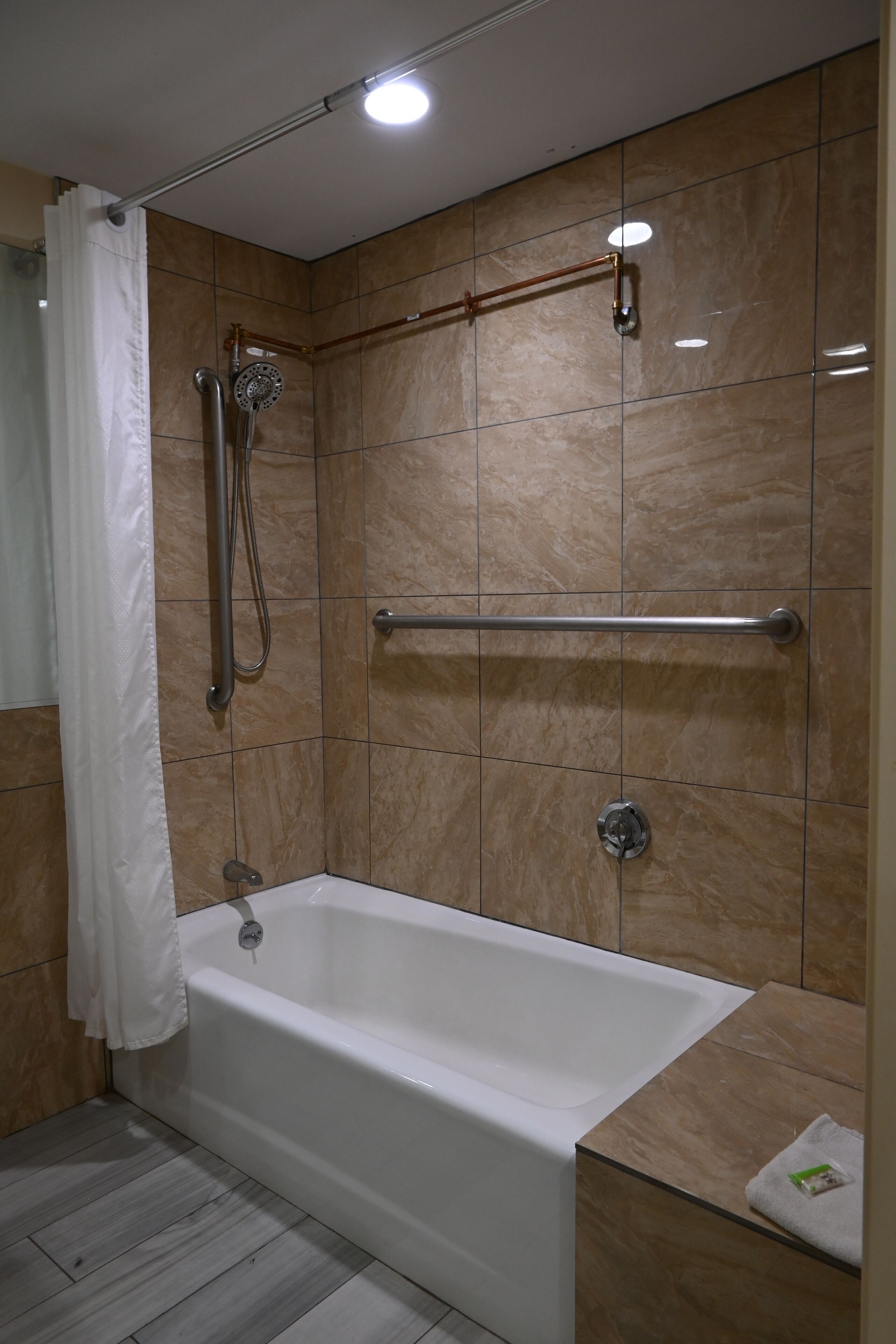 Un baño moderno con bañera, ducha y un cabezal de ducha manual, además de una barra de apoyo.