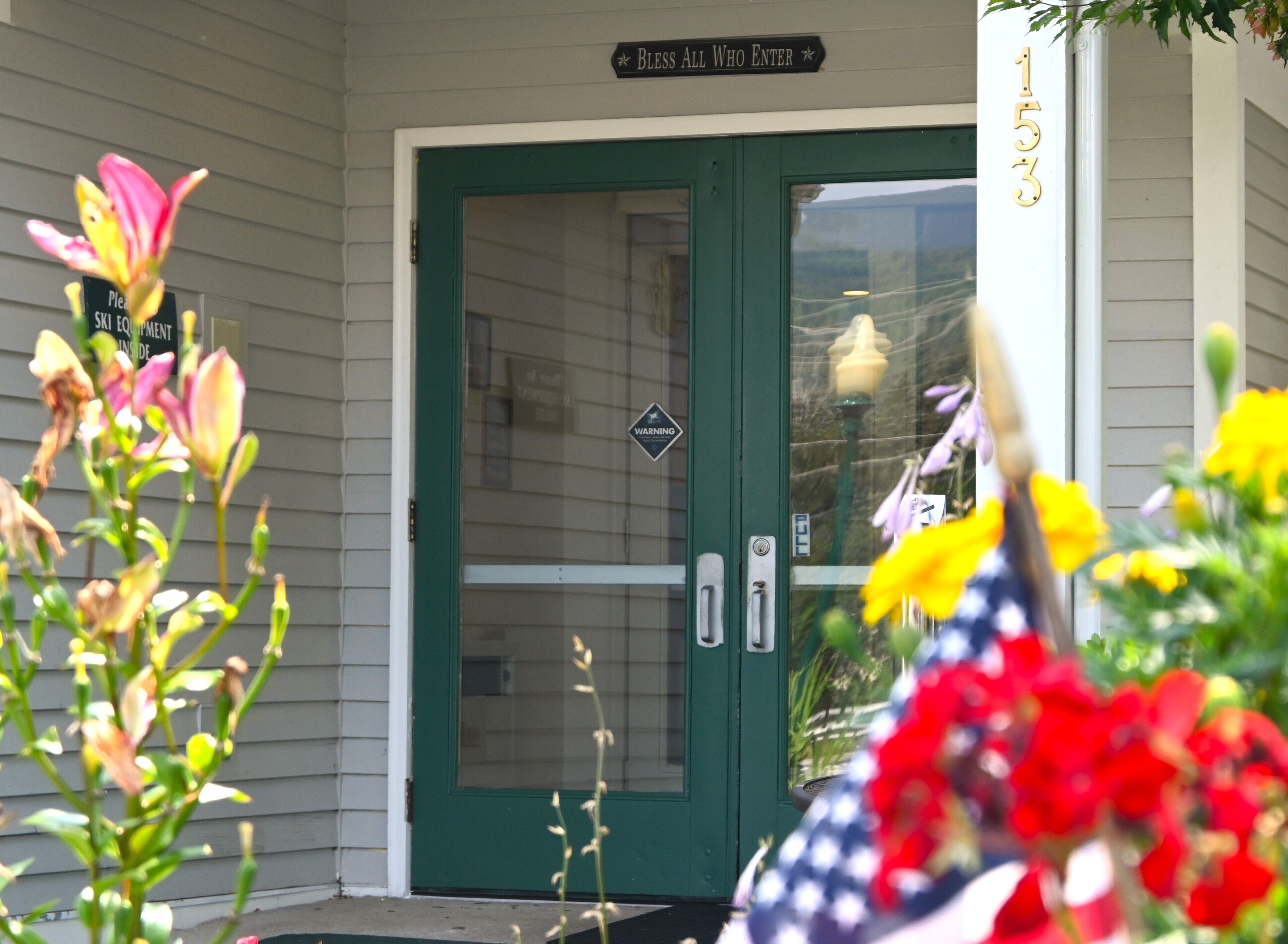 A green door with a sign above it that reads "Bless All Who Enter."