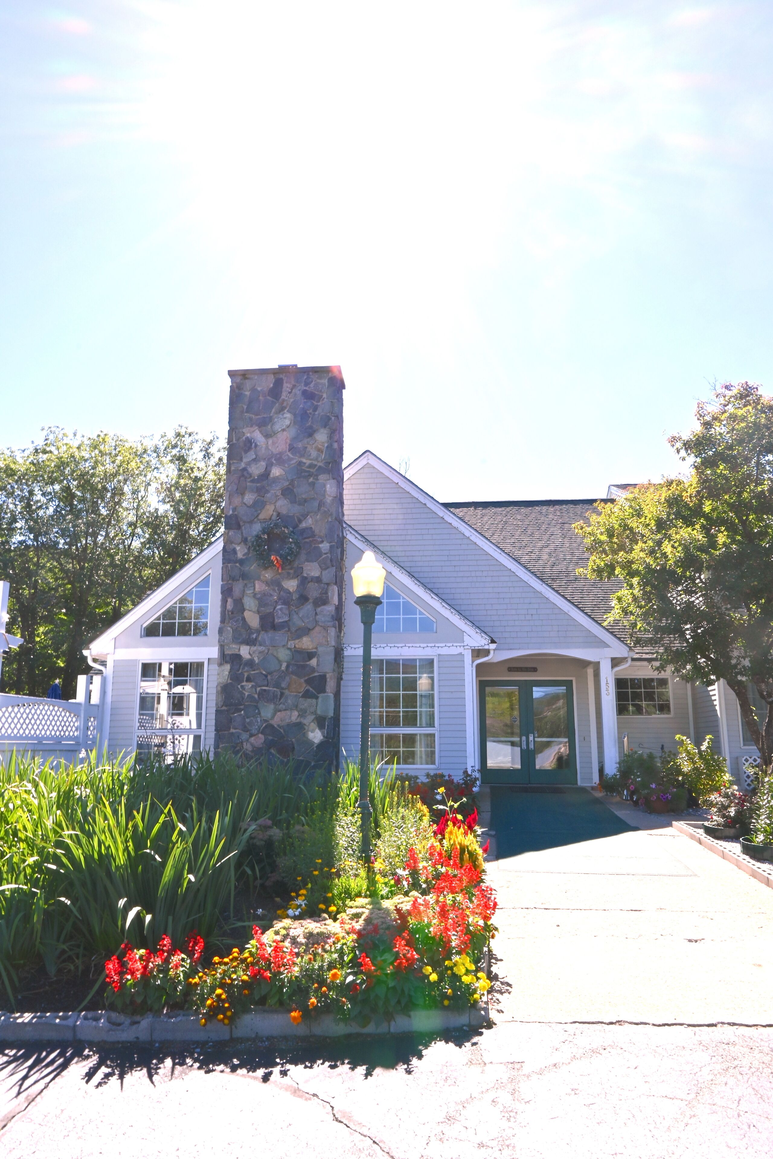 A house with a stone pillar, a front porch, and a garden with red and yellow flowers.