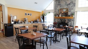 A restaurant with wooden tables and chairs, a stone fireplace, and a kitchen area with appliances and decorations. - The Lodge At Jackson Village (Jackson)