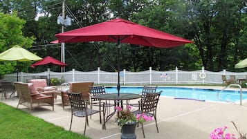 Un espace extérieur aménagé en terrasse avec une piscine, entouré d’une clôture blanche en bois, comprenant des meubles en osier et des parasols rouges.
