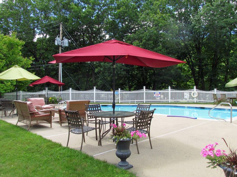 Un espace extérieur aménagé en terrasse avec une piscine, entouré d’une clôture blanche en bois, comprenant des meubles en osier et des parasols rouges.
