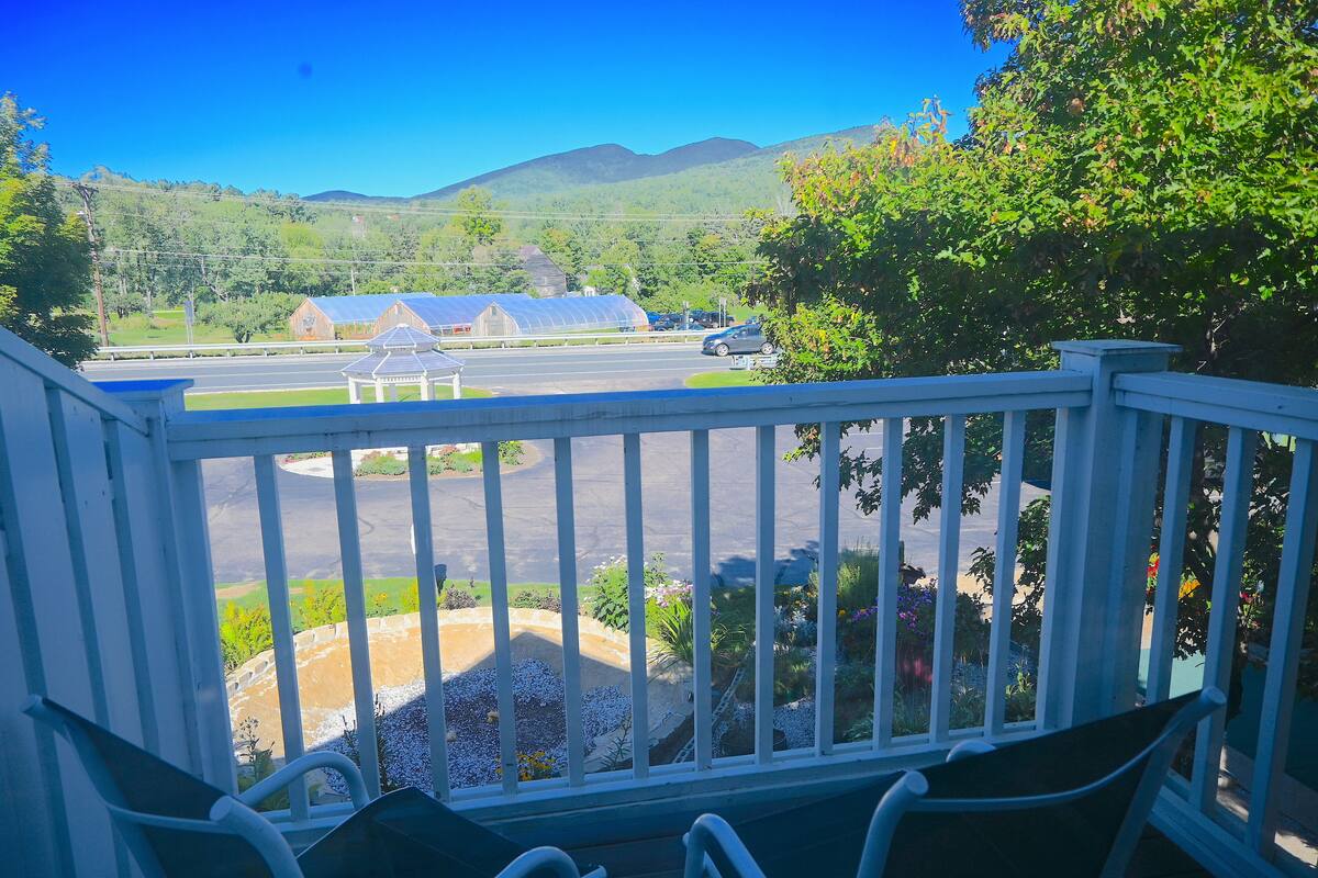 A balcony with a view of a road, green fields, and distant mountains.