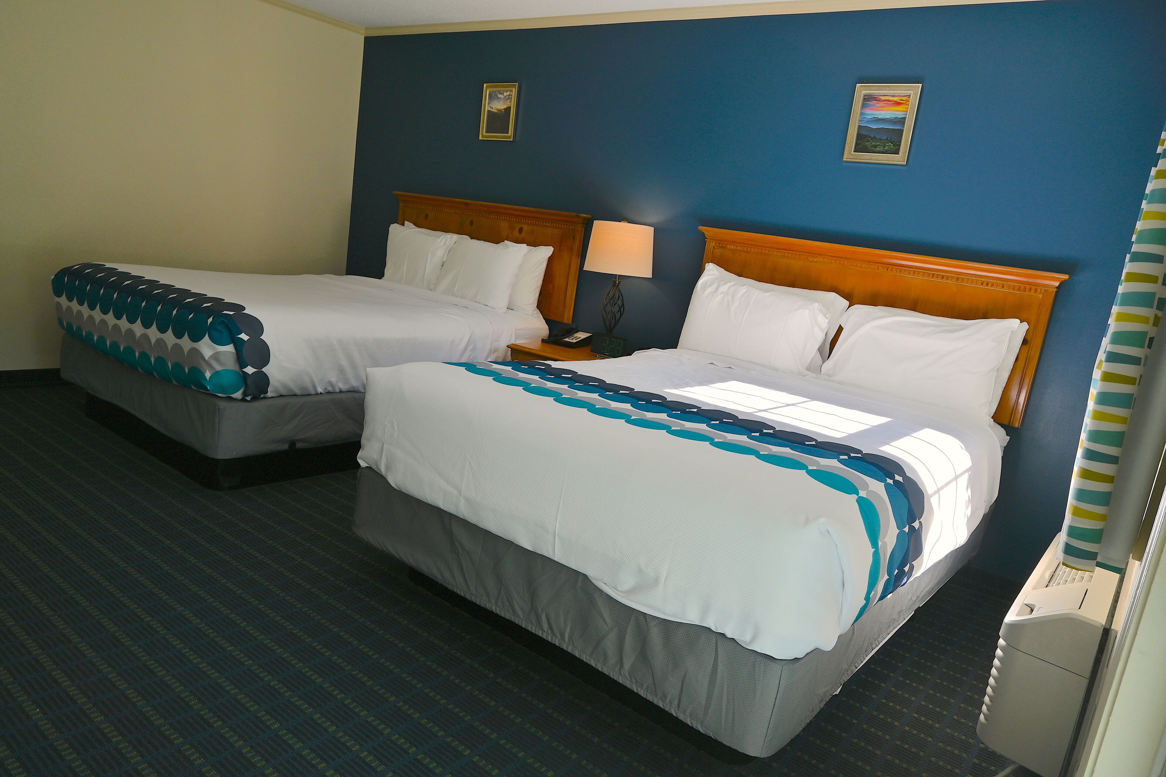 Habitación de hotel con dos camas, una mesita de noche, una lámpara y una ventana con cortinas.