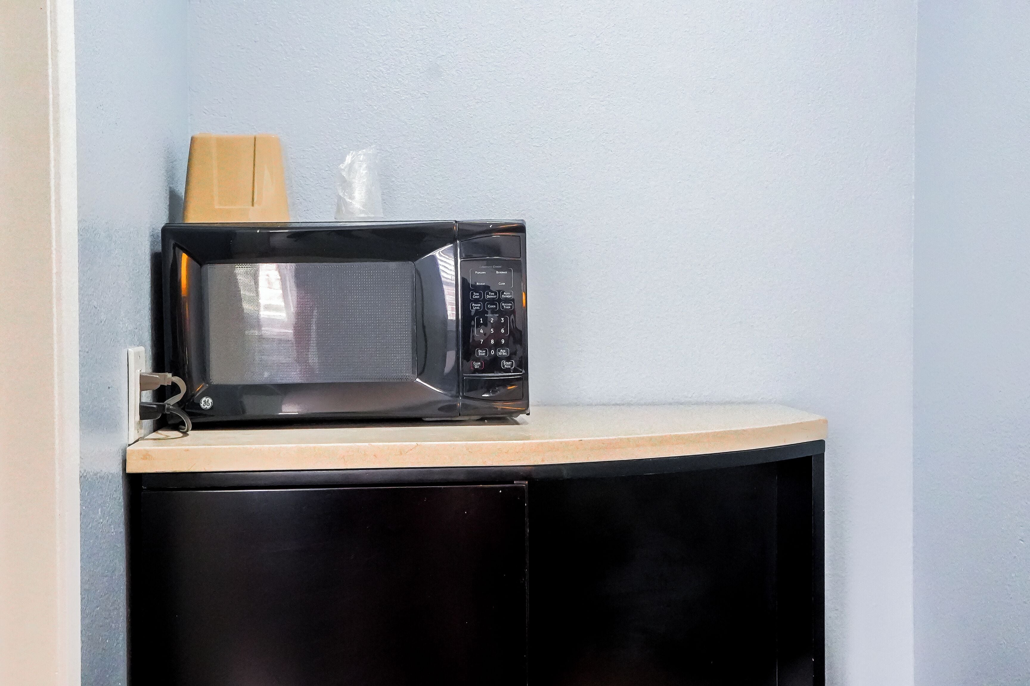 A microwave on a countertop with a wooden block and a plastic bag.