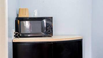 A microwave on a countertop with a wooden block and a plastic bag.