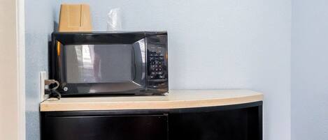 A microwave on a countertop with a wooden block and a plastic bag.