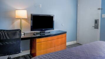 A hotel room with a bed, a desk with a television, a chair, and a door.
