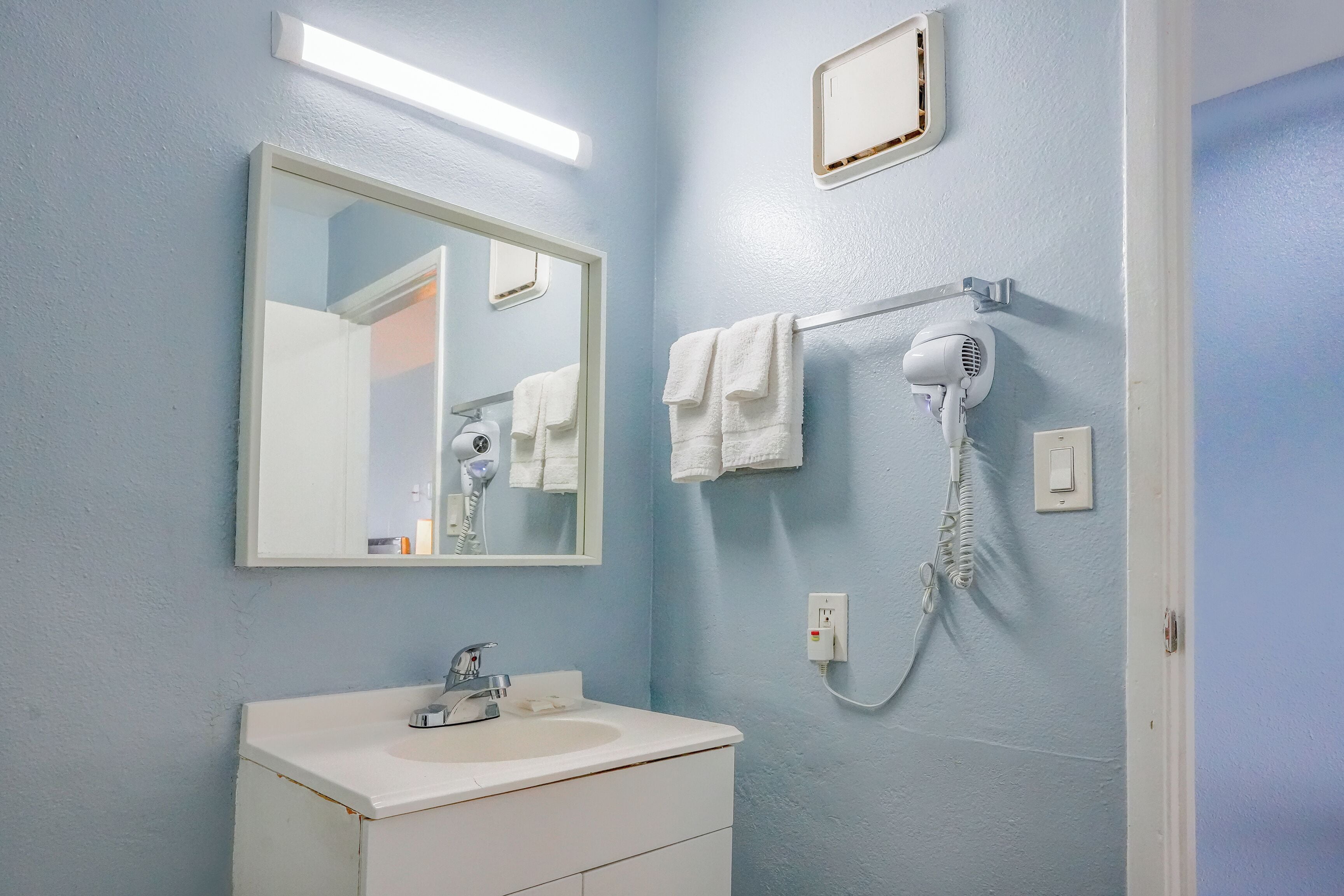 Un baño con un lavabo blanco, un espejo, un secador de pelo y un perchero para toallas.