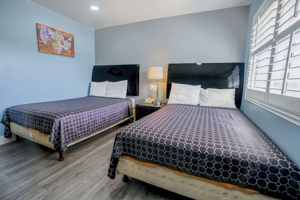 A hotel room with two beds, a wooden floor, a wall map, and a window with blinds.