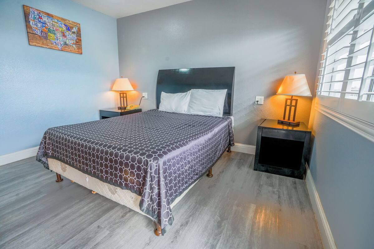 A neatly made bed with a patterned bedspread, two bedside tables with lamps, a wall map, and a window with blinds.