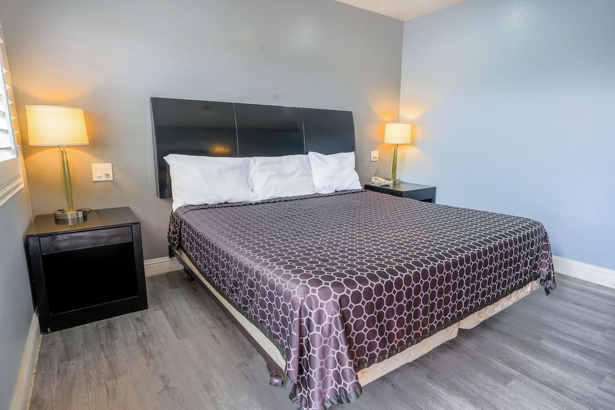 A hotel room with a large bed, two bedside tables, a headboard, and two wall-mounted lamps.