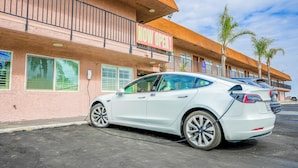 Ein weißes Tesla-Auto vor einem Gebäude mit einem 'NOW OPEN'-Schild.